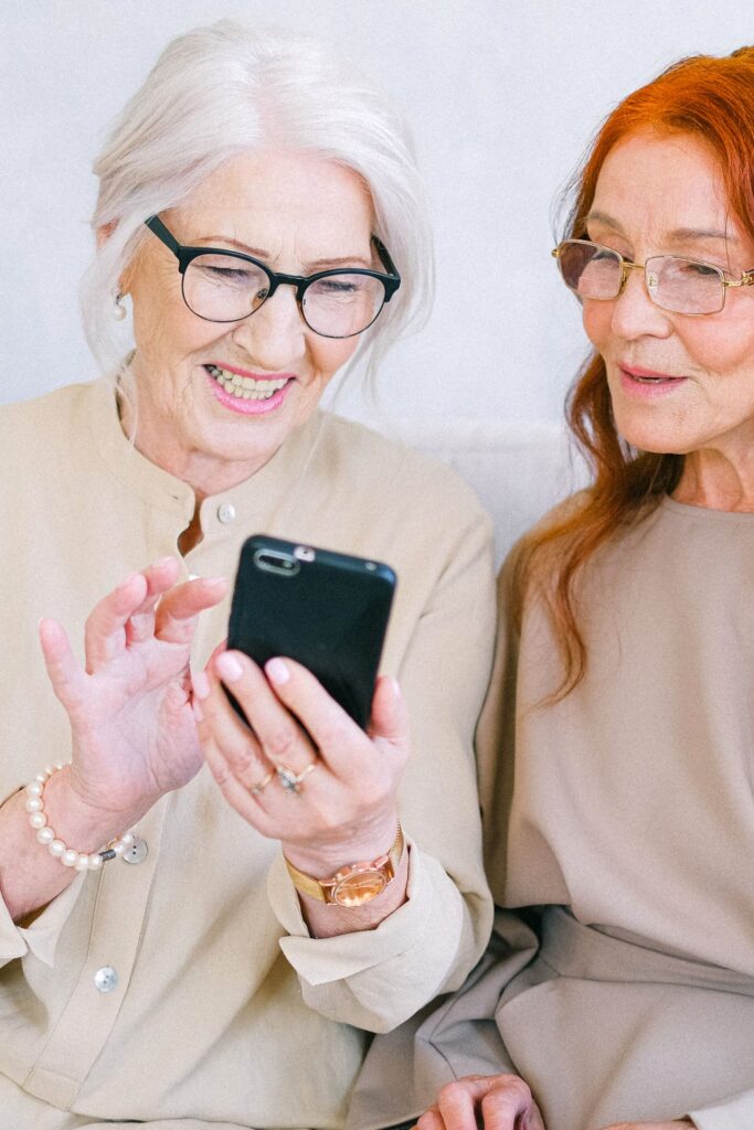 Deux personnes âgées souriantes consultent ensemble une application sur smartphone, illustration de la transition vers des aide-mémoire numériques