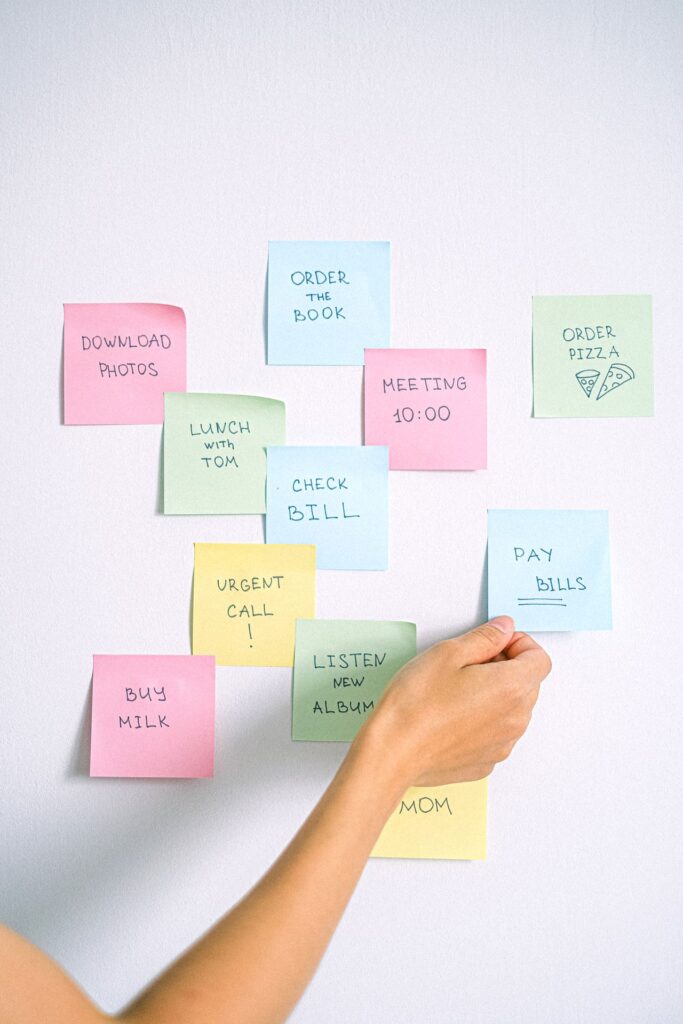 Main qui accroche un post-it parmi plusieurs notes colorées sur un mur, exemple d'aide-mémoire traditionnel utilisé au quotidien